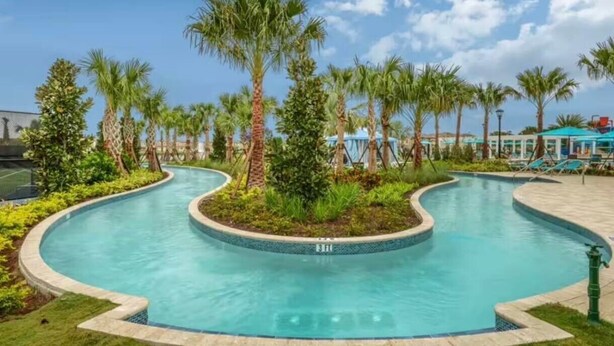 Une piscine incurvée, bordée de palmiers et dotée d’un espace salon abrité.