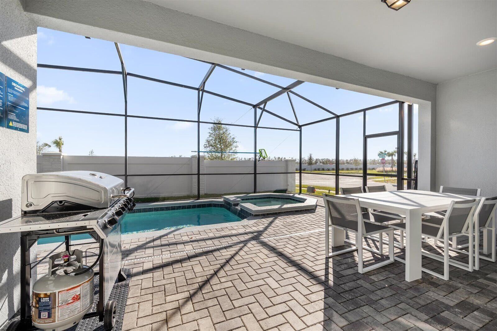 A covered outdoor pool area with a hot tub, a barbecue grill, and a table with chairs.