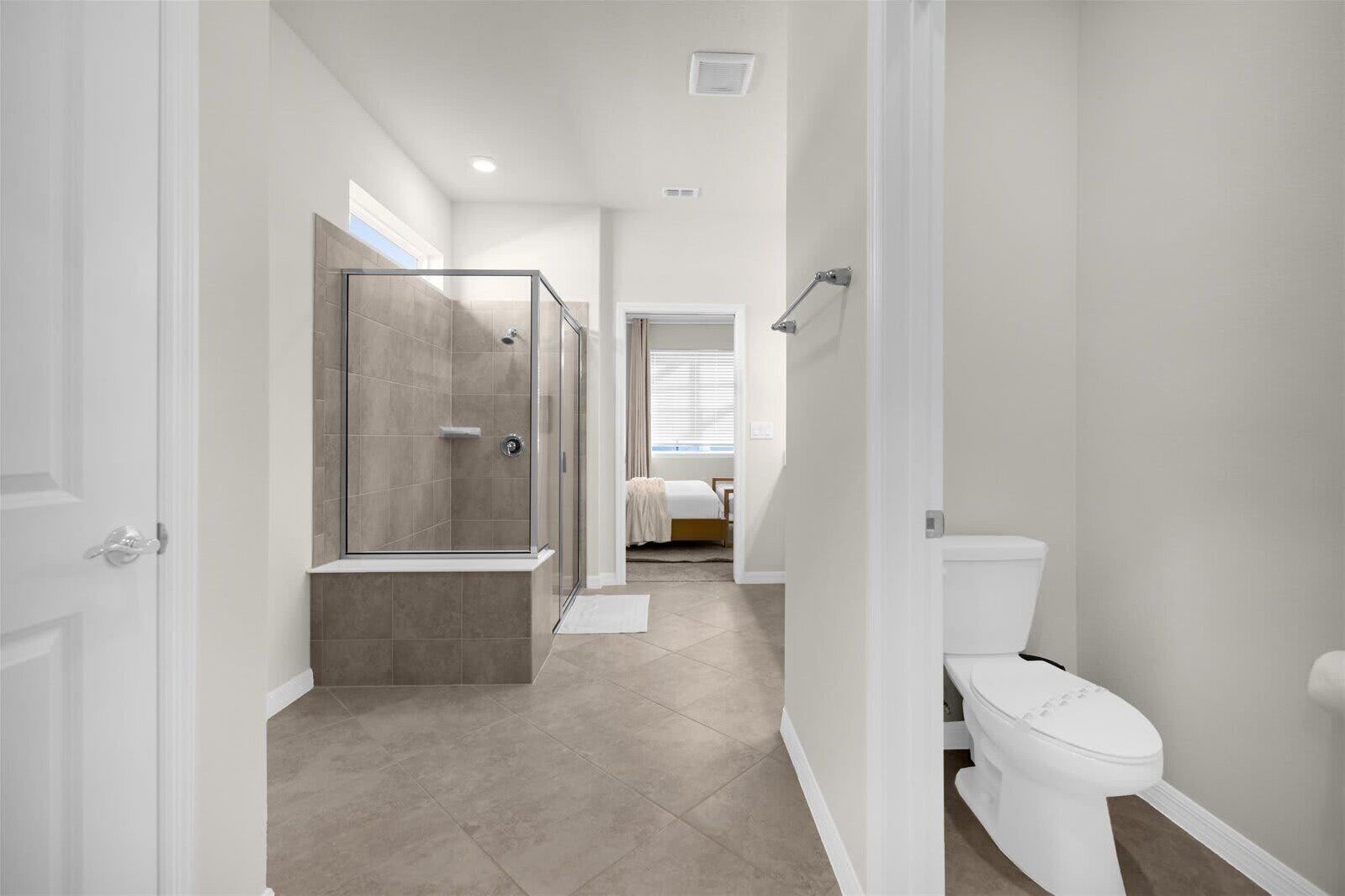 Une salle de bain moderne avec une douche à parois de verre, des toilettes et un lit en arrière-plan.