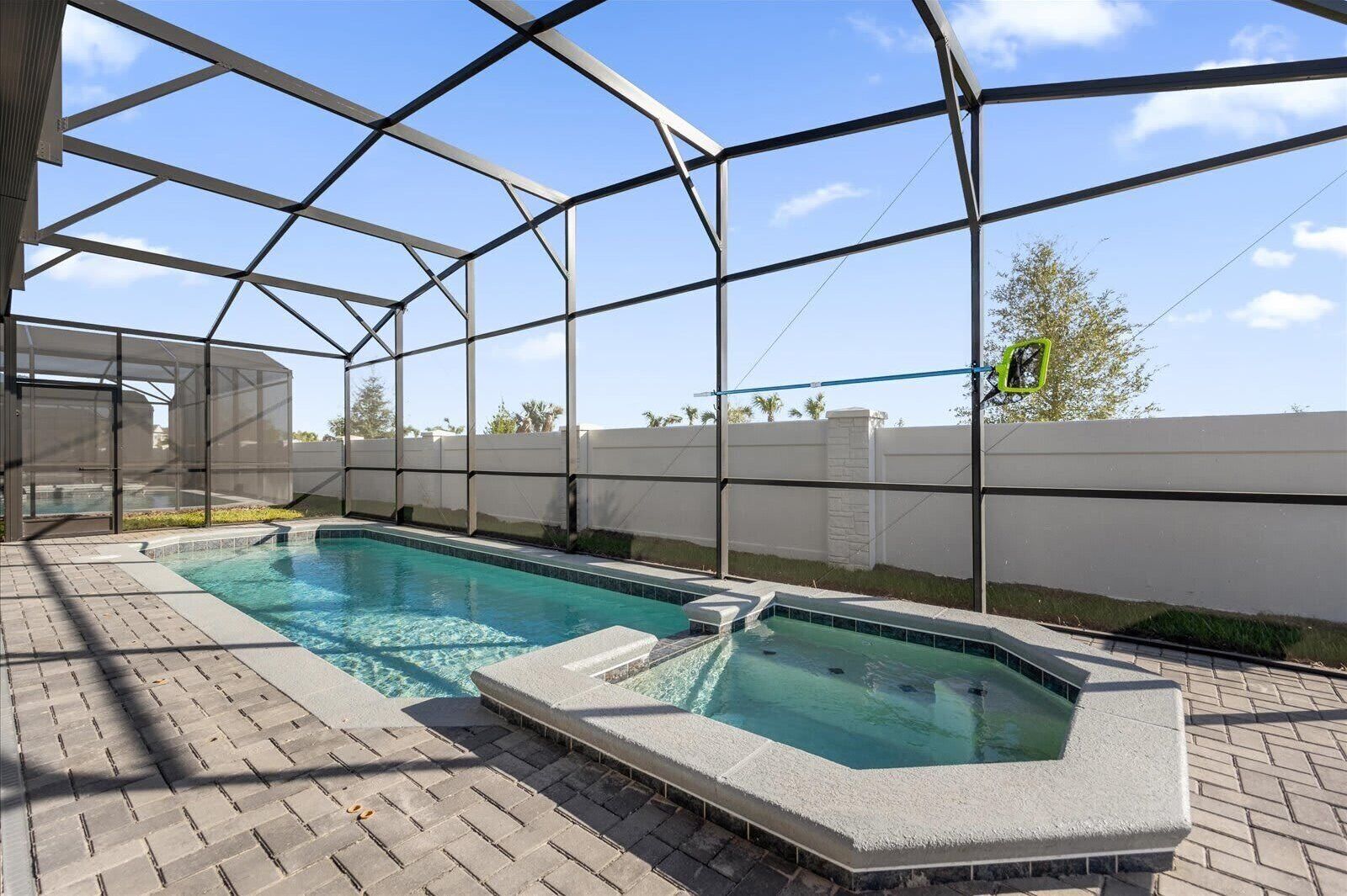 Ein Pool mit Glasveranda, umgeben von einer gepflasterten Terrasse und einer weißen Mauer.