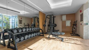 A modern gym with weightlifting equipment, a rack of dumbbells, and a mirror. - Stayshort - Contemporary Studio With Open Layout in JVC (Dubai)