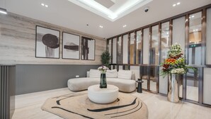 A modern living room with a round coffee table, a beige sofa, and a large window with a view. - Stayshort - Contemporary Studio With Open Layout in JVC (Dubai)