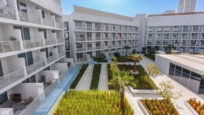 A modern multi-story hotel with balconies, a central courtyard with plants, and a clear sky. - Stayshort - Contemporary Studio With Open Layout in JVC (Dubai)