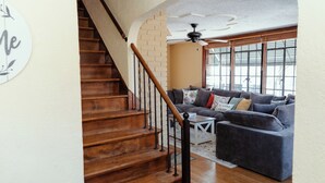 A staircase with wooden steps and a black handrail, leading to a living room with a gray sofa and a white coffee table. - Quaint & Cozy Indiana Style (Shelbyville)