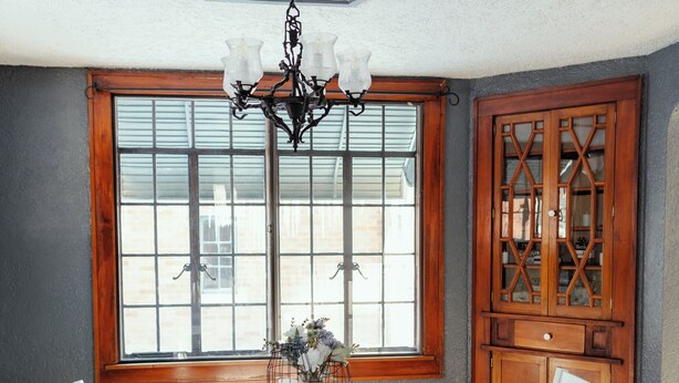 A dining room with a table and chairs, a chandelier, a window with a view, and a wooden cabinet. - Quaint & Cozy Indiana Style (Shelbyville)