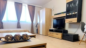 Habitación de hotel moderna con una cama, un televisor, un aparador de madera y una mesa con adornos.