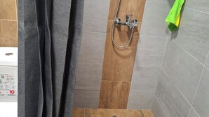 Un área de ducha con suelo de madera, un cabezal de ducha y pared de azulejos.
