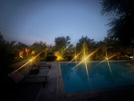 Ein Poolbereich bei Nacht mit freiem Blick auf den Pool, umgeben von Bäumen und einem Gebäude mit warmer Beleuchtung.
