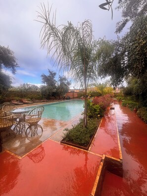 Una piscina con cubierta roja, rodeada de abundante vegetación y un cielo despejado.
