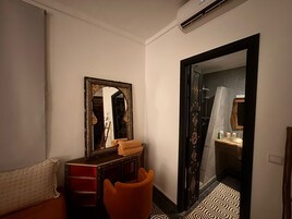 A hotel room with a large mirror, a wooden dresser, a chair, and a patterned floor.