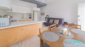 A modern kitchen with white cabinets, a wooden dining table, and a grey sofa. - Downtown Apt w/common pool + private terrace (La Paz)