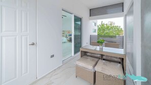 A modern room with a glass door leading to an outdoor area, a glass-top table with wicker chairs, and a view of greenery outside. - Downtown Apt w/common pool + private terrace (La Paz)