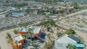 An aerial view of a coastal resort area with multiple buildings, including a prominent orange structure with a pool and a sign for La Paz Rentals.