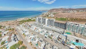 Vista aerea di una zona costiera con un complesso alberghiero, comprendente diversi edifici e una spiaggia.