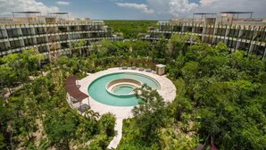Een resort met een centraal gelegen, rond zwembad, omgeven door weelderige begroeiing en moderne gebouwen.