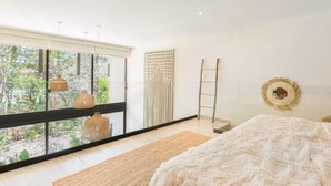 Een moderne slaapkamer met een groot raam, een bed, een ladder en een decoratief wandobject.