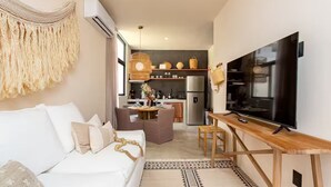 A modern living room with a white sofa, a TV on a wooden stand, and a kitchen in the background. - Exquisitely Decorated 2 BD Retreat in Tulum (Tulum)