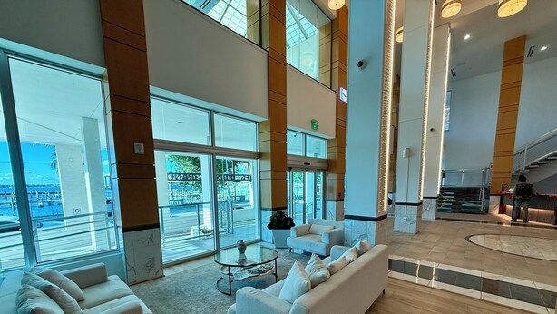 Um hall amplo com área de estar espaçosa, parede de vidro com vista para o porto de iates e escadaria moderna.
