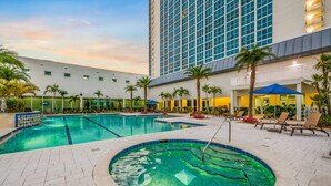 Uma área de piscina de hotel com uma piscina grande, espreguiçadeiras e palmeiras.