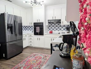 A modern kitchen with white cabinets, a black refrigerator, a coffee maker, and a patterned rug. - Bird's Nest 3 BR/2 bath home 5 min from base (Enterprise)