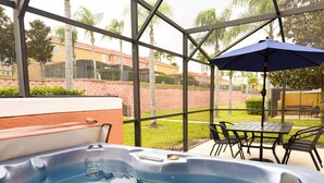 Un jacuzzi con mesa y sillas, una sombrilla y vistas a un barrio residencial con casas y palmeras.