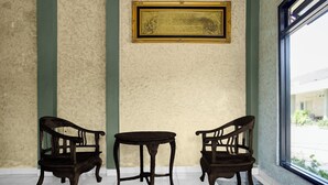 Ein Zimmer mit zwei Holzstühlen und einem kleinen Tisch, einem gerahmten Bild an der Wand und einem Fenster mit Blick nach draußen.