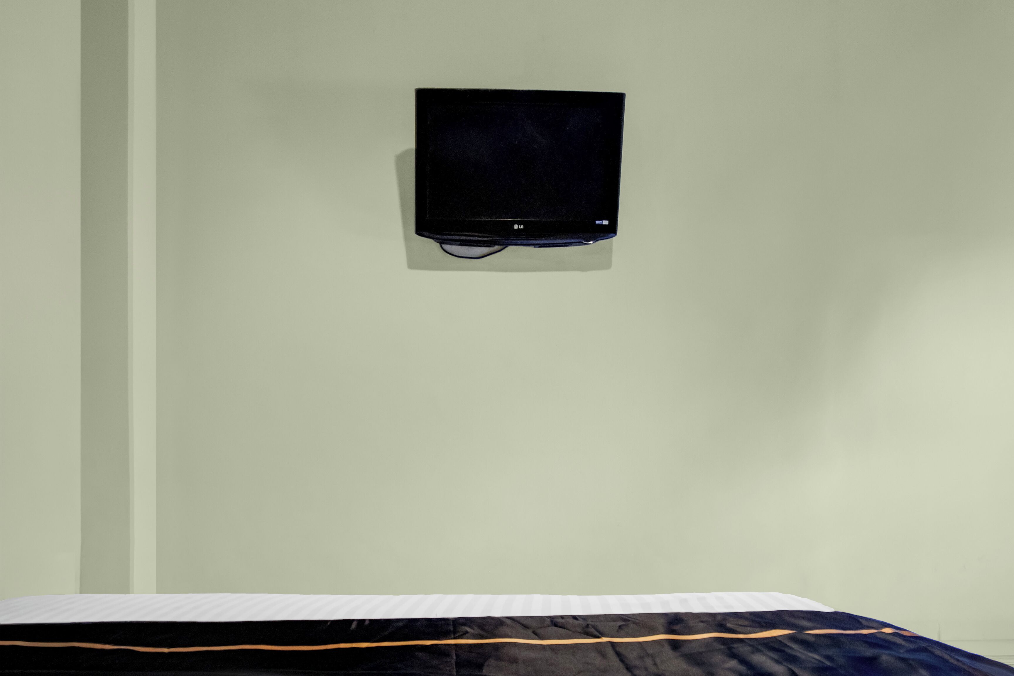 A room with a bed, a wall-mounted TV, and a plain wall.