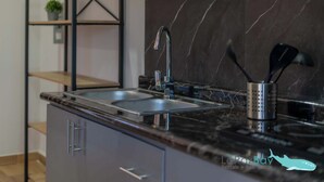 Una cocina moderna con encimera de mármol negro, pileta de acero inoxidable y un organizador metálico para utensilios.