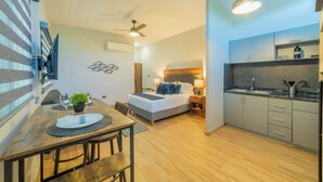 Habitación de hotel pequeña con cama, mesita de noche y kitchenette.