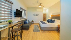 Un espacio habitable compacto con una cama, un sofá, una zona de comedor y un televisor montado en la pared.
