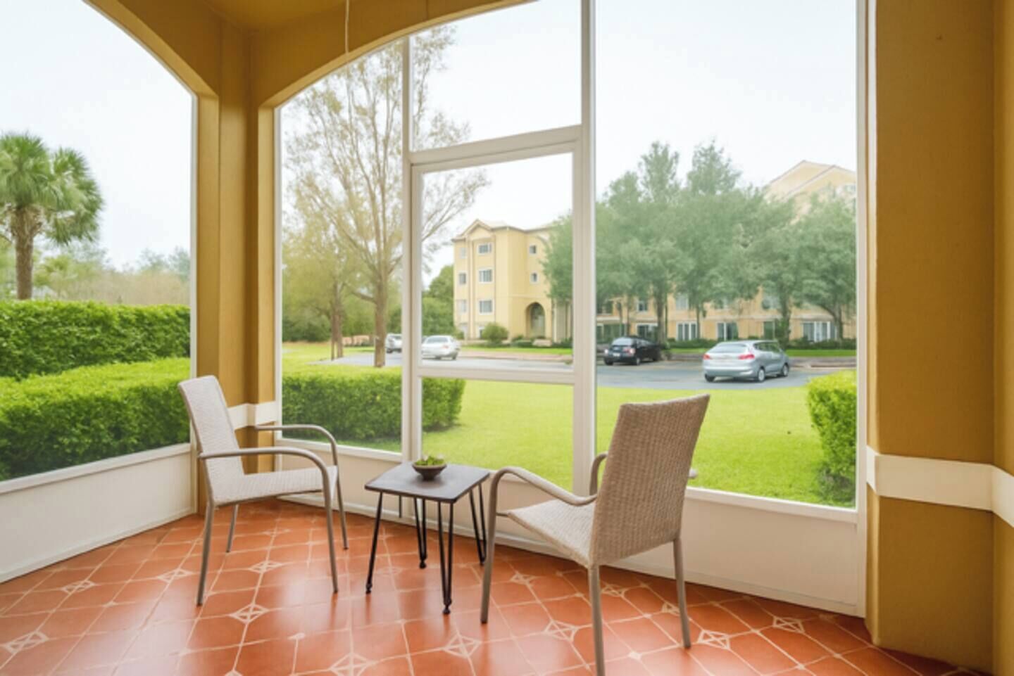 A balcony with two chairs and a small table, overlooking a well-maintained lawn and a building in the background.