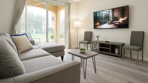 Ein modernes Wohnzimmer mit einer Couch, zwei Sesseln, einem Couchtisch und einem Fernseher auf einem Schrank.
