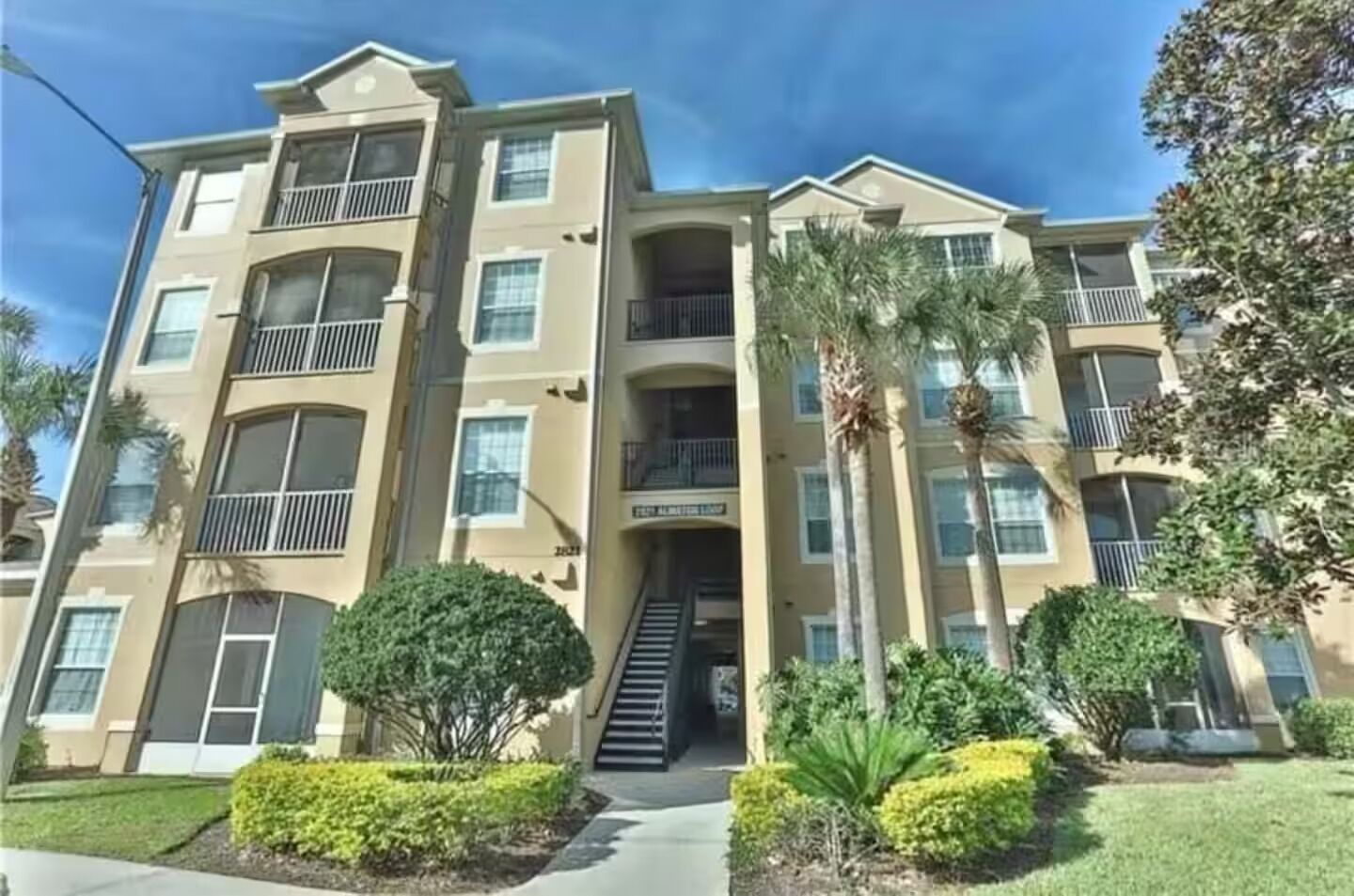 A multi-story building with balconies, a central staircase, and well-maintained landscaping.
