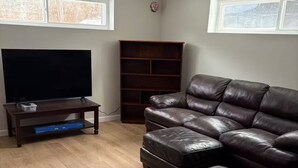 A living room with a leather sofa, a television, and a wooden bookshelf. - Okemo House (Ludlow)