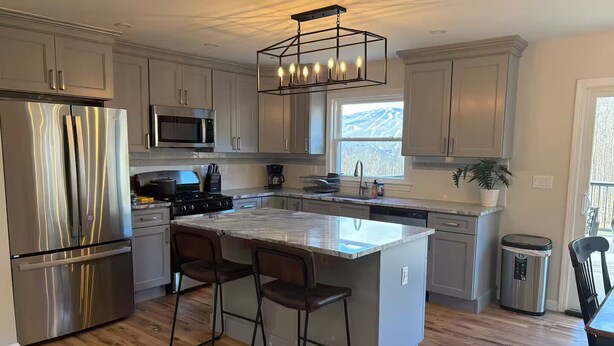 A modern kitchen with stainless steel appliances, a marble island, and bar stools. - Okemo House (Ludlow)