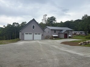 A two-story building with a garage, a covered porch, and a stone foundation. - Okemo House (Ludlow)