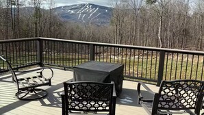 A deck with two rocking chairs and a table, overlooking a forest and mountains. - Okemo House (Ludlow)