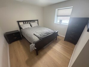 A bedroom with a bed, a nightstand, a dresser, and a window. - Okemo House (Ludlow)