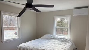 A bedroom with a bed, two windows, a ceiling fan, and an air conditioning unit. - Okemo House (Ludlow)