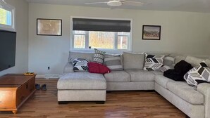 A living room with a sectional sofa, a wooden coffee table, and a ceiling fan. - Okemo House (Ludlow)