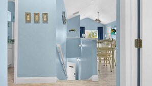 Une pièce avec un mur bleu clair, une porte blanche, un plafond blanc et un coin repas avec des chaises et une table en bois.