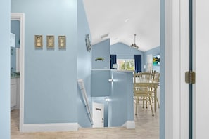 Une pièce avec un mur bleu clair, une porte blanche, un plafond blanc et un coin repas avec des chaises et une table en bois.