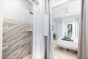 Ein modernes Badezimmer mit Dusche, Toilette und Waschbecken. Ein Bett mit Kissen und ein Fenster mit Vorhängen.