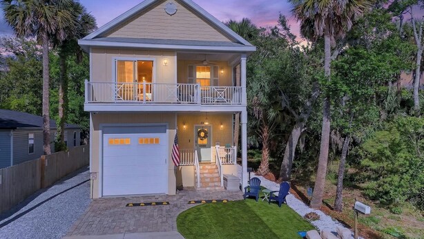 Une maison à deux étages avec un garage, un balcon et une véranda à l’avant, équipée de sièges pour l’extérieur.
