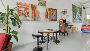 Une pièce avec une table d’échecs, des œuvres d’art accrochées aux murs, une plante et un ventilateur.
