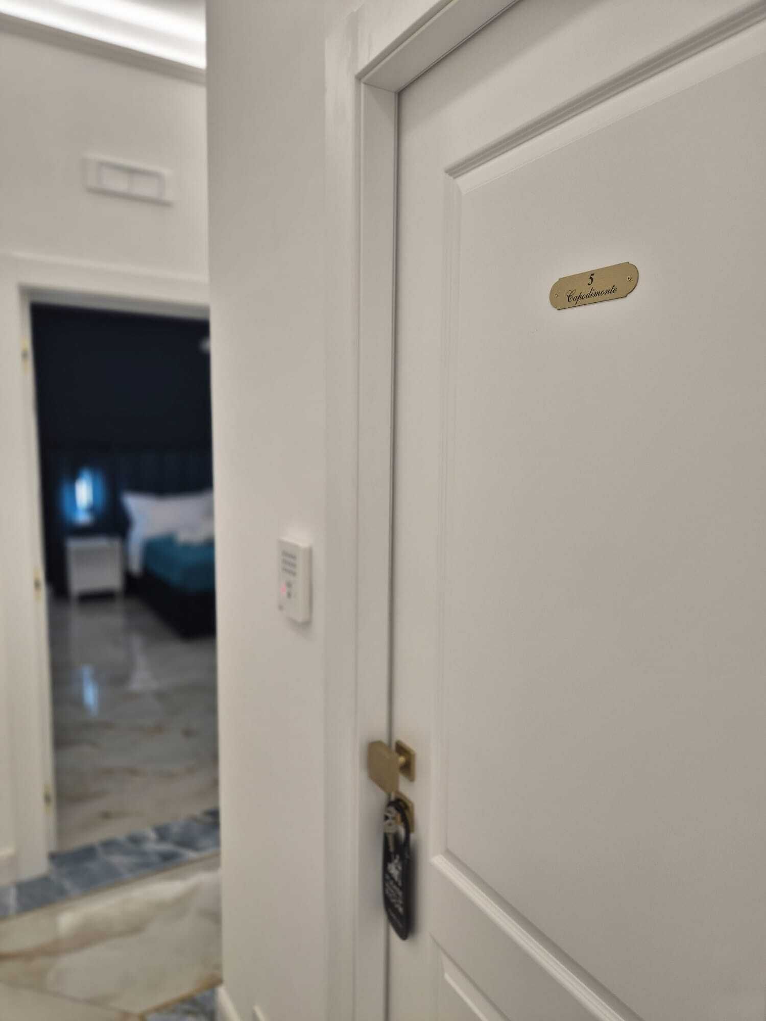 A hotel room with a white door, a keycard lock, and a sign indicating room number 5.