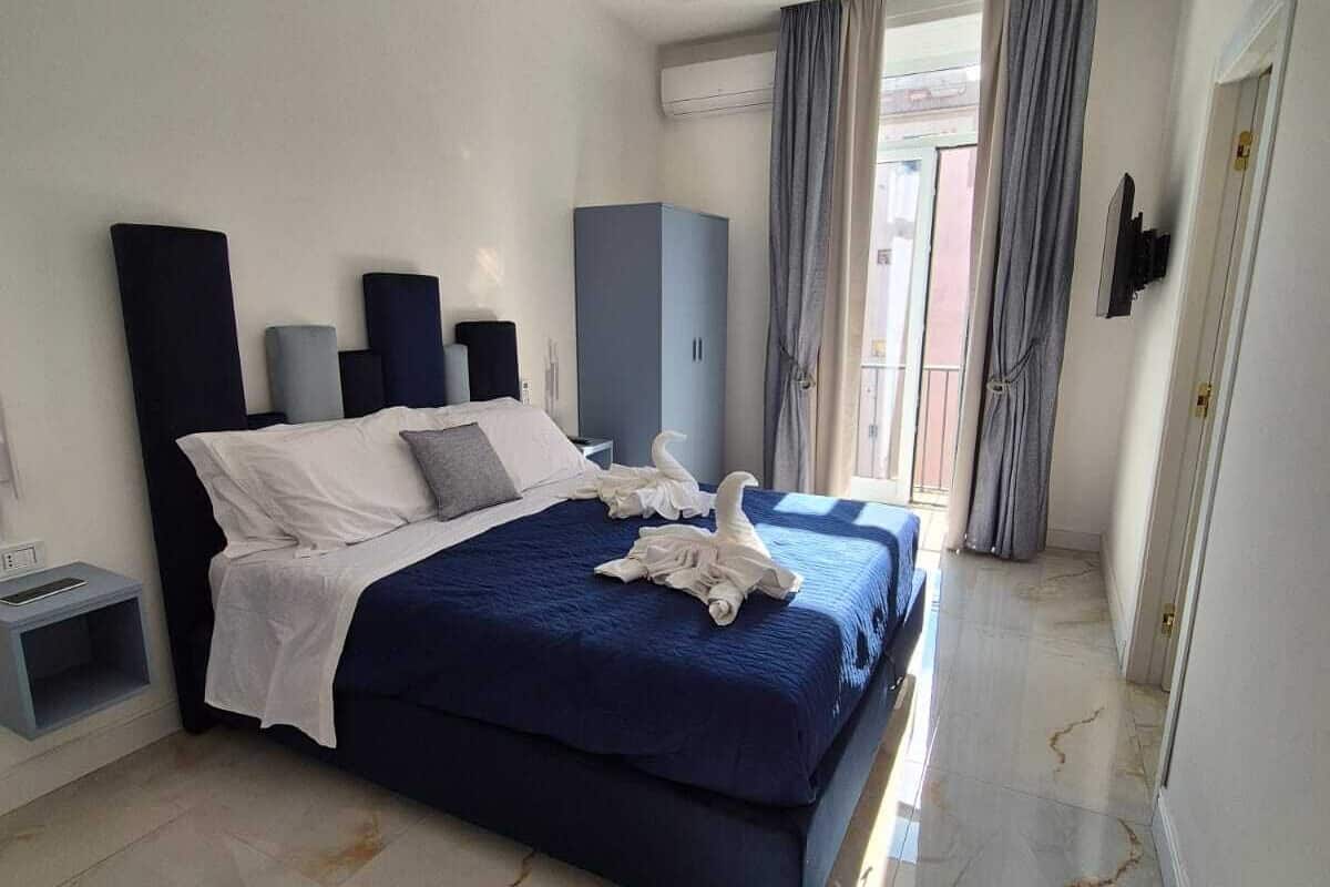 A modern hotel room with a large bed, a wardrobe, and a small bedside table.