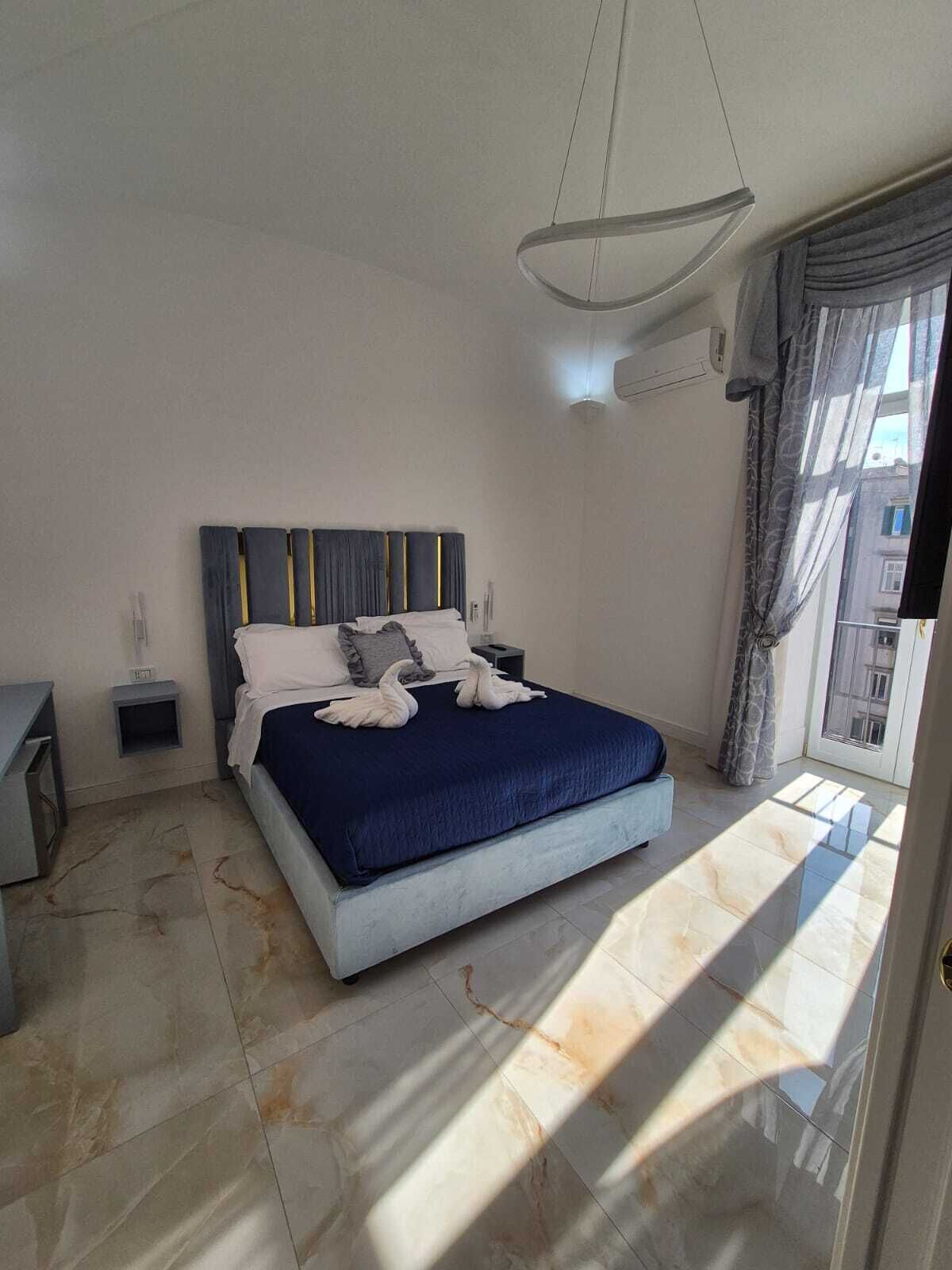 Quarto moderno com uma cama grande, mesas de cabeceira, luminária pendente e vista para o exterior.