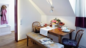 A dining area with a wooden table, chairs, and a bench. There is a window with curtains, a wall-mounted light fixture, and a door with a coat rack. - KÖNIGSschlaf's barrier-free apartment: Chic, spacious, central! (Konstanz)