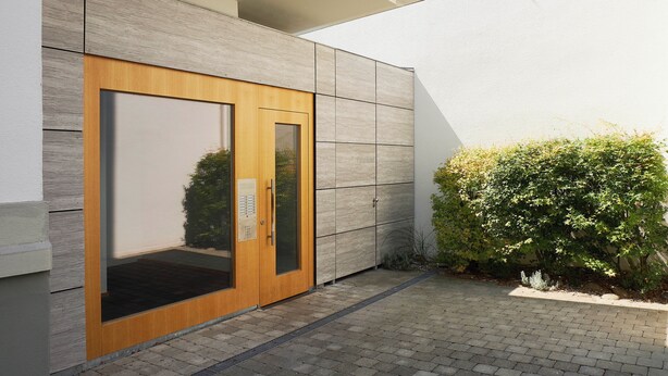 A modern building exterior with a wooden door and a small garden area. - KÖNIGSschlaf's barrier-free apartment: Chic, spacious, central! (Konstanz)